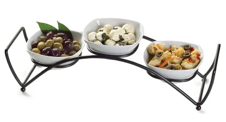 A black metal stand holds three white bowls filled with assorted appetizers: green and black olives, mozzarella balls with herbs, and marinated vegetables with olives.