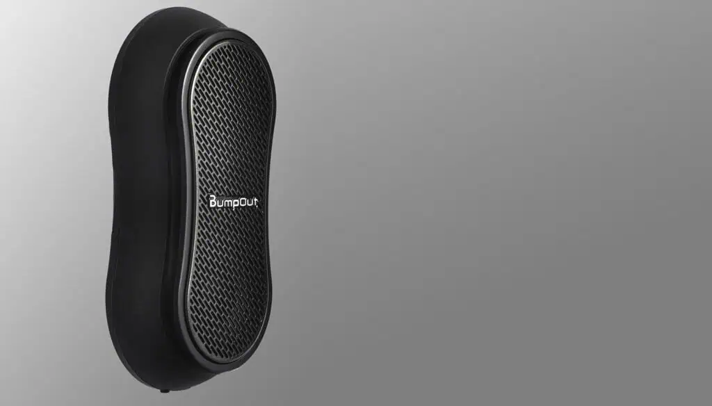 A black, oval-shaped portable speaker with a mesh front and the logo BumpOut in white, displayed against a gradient gray background.