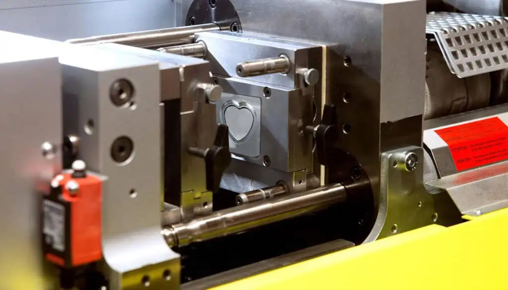 Close-up of an industrial machine with a metal mold featuring a heart-shaped cavity, used in a manufacturing or injection molding process.
