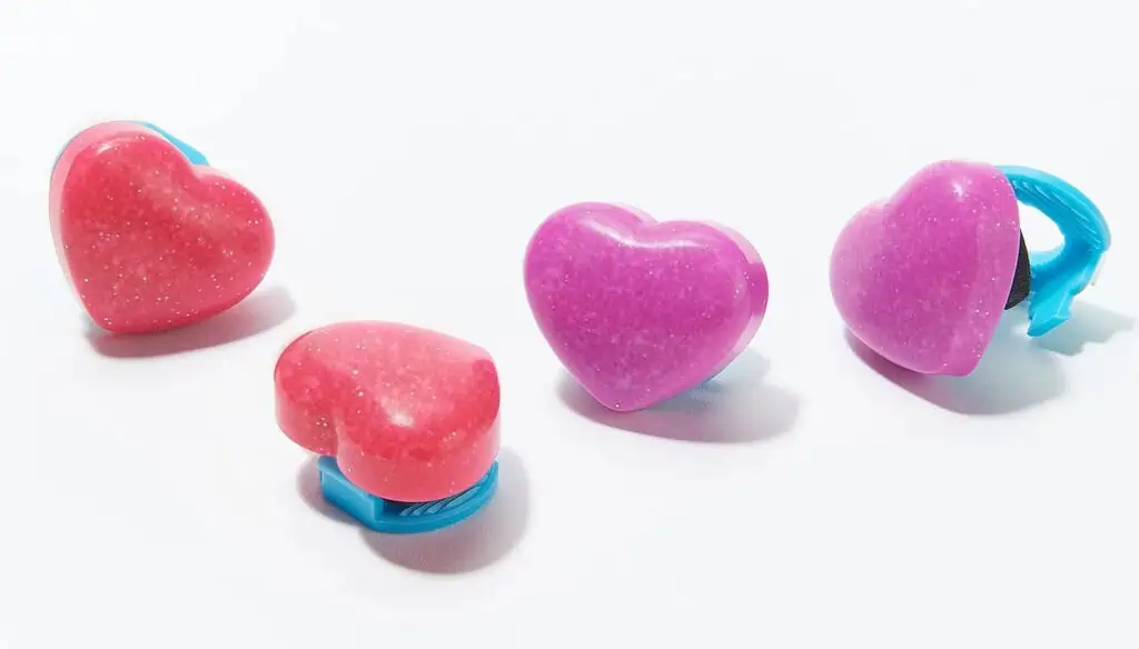 Four plastic heart-shaped hair clips, two pink and two purple, with blue clasps, are arranged on a white background.