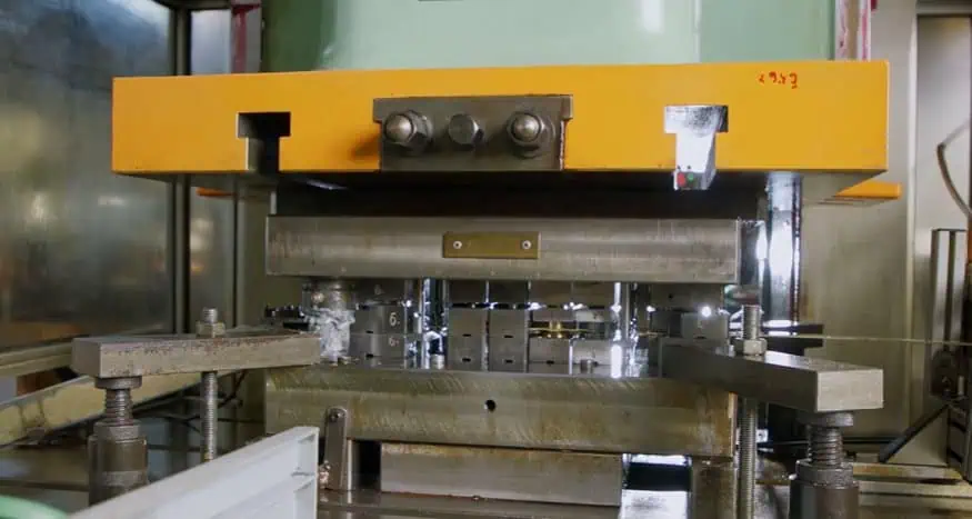A close-up view of an industrial metal stamping machine in operation, pressing down on a metal sheet to form parts inside a factory setting.