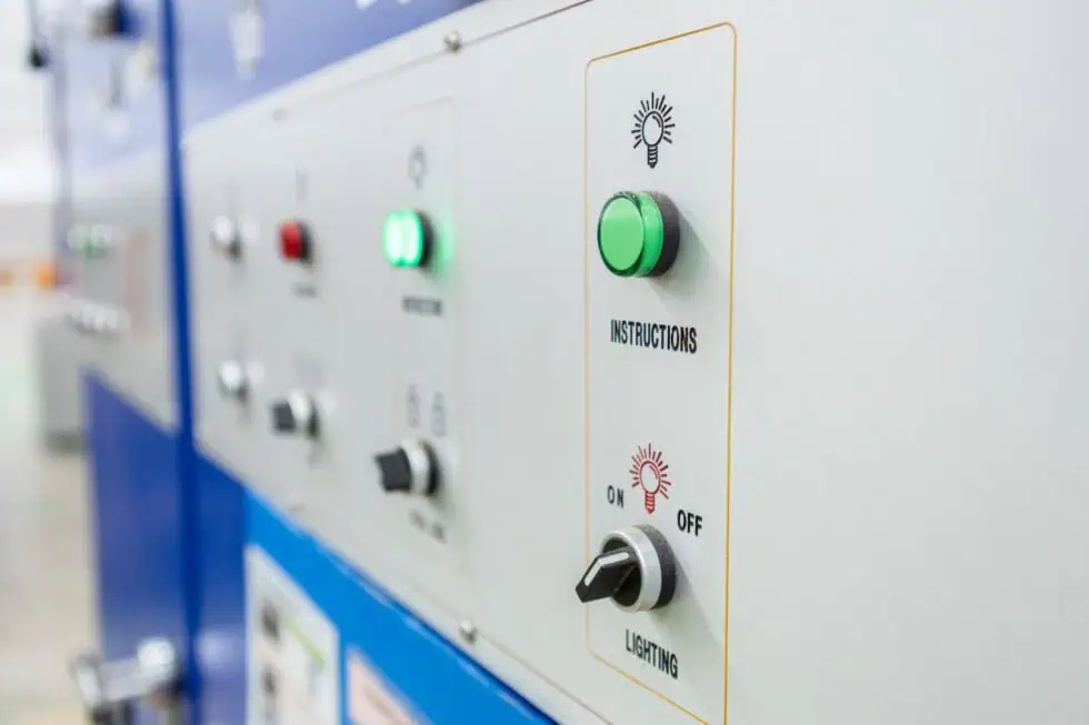Close-up of an industrial control panel with labeled buttons, indicator lights, and switches, including a green INSTRUCTIONS button and a section for LIGHTING with on/off options.