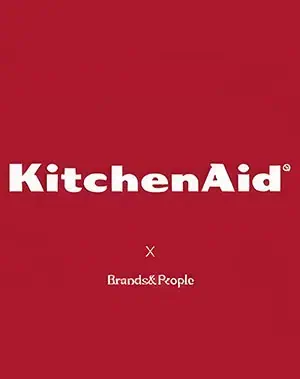 White KitchenAid logo on a red background with the text Brands&People in smaller font below, separated by an x symbol, indicating a collaboration.