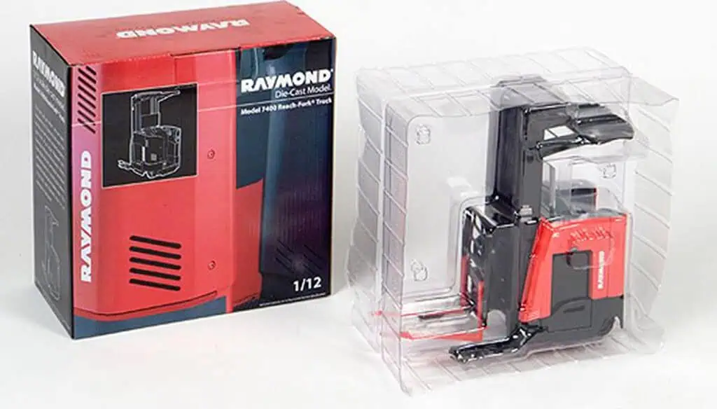 A die-cast model of a Raymond reach forklift is displayed inside clear plastic packaging next to its red and black retail box, which features an image of the forklift and branding.