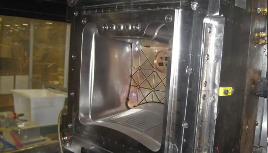 A close-up view of a large, metallic, industrial-grade vacuum chamber with an open door, exposing its clean, angular interior and various mechanical components.