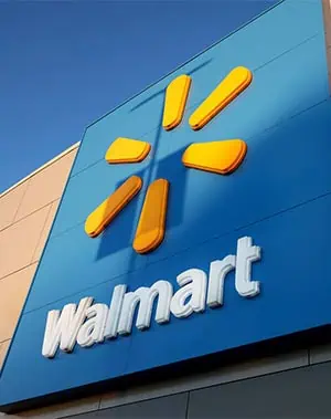 A large blue Walmart sign with the yellow spark logo and white Walmart text is mounted on the exterior of a building against a clear blue sky.